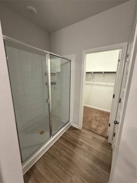 Glass-enclosed shower with white subway tile surround, integrated shelving, and wood-finish flooring