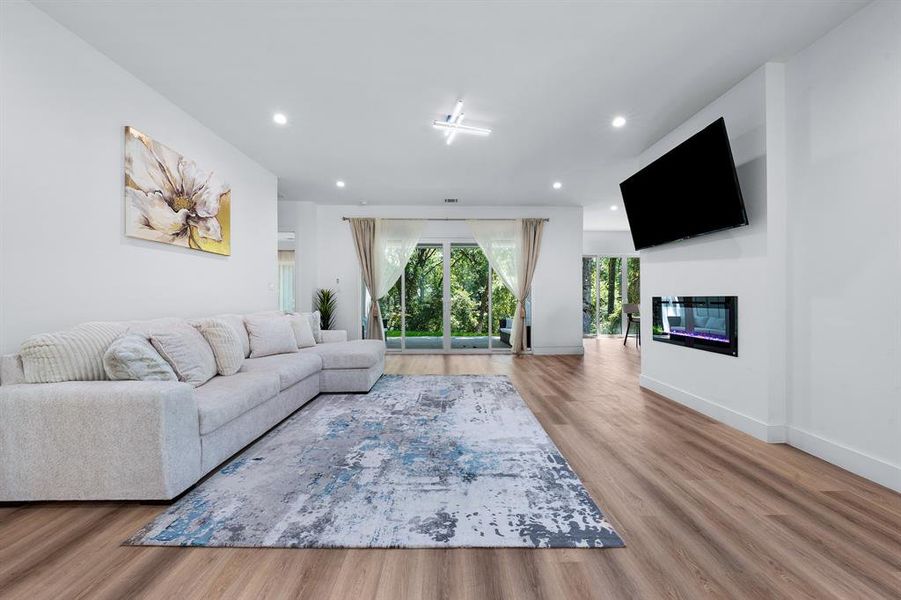 Living room with a glass covered fireplace, light wood-style flooring, and recessed lighting Living room with a glass covered fireplace, light wood-style flooring, and recessed lighting