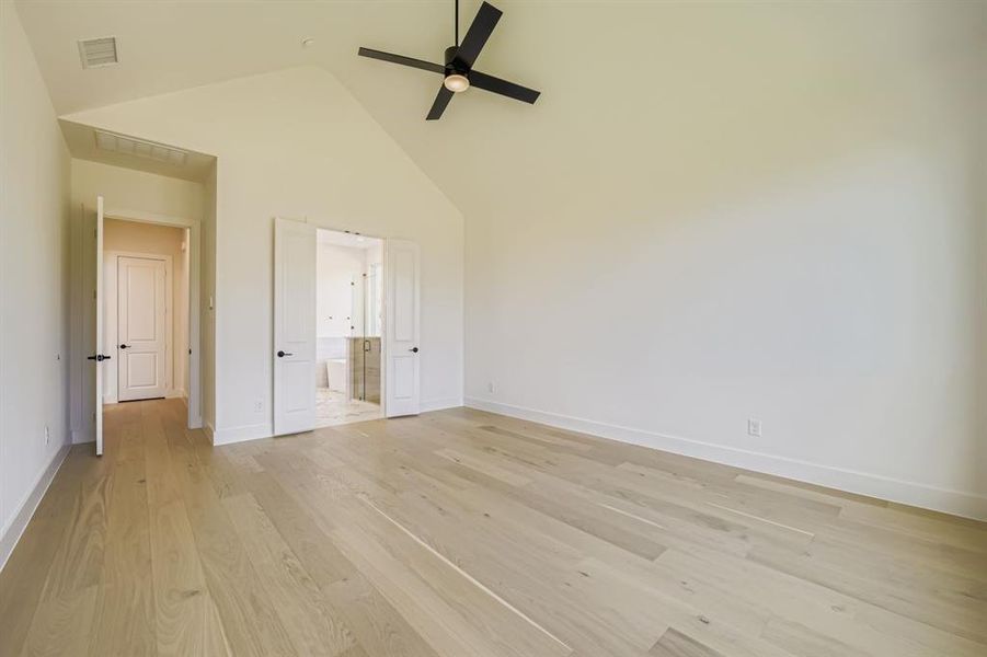 Unfurnished bedroom with high vaulted ceiling, connected bathroom, light wood-type flooring, and ceiling fan Unfurnished bedroom with high vaulted ceiling, connected bathroom, light wood-type flooring, and ceiling fan