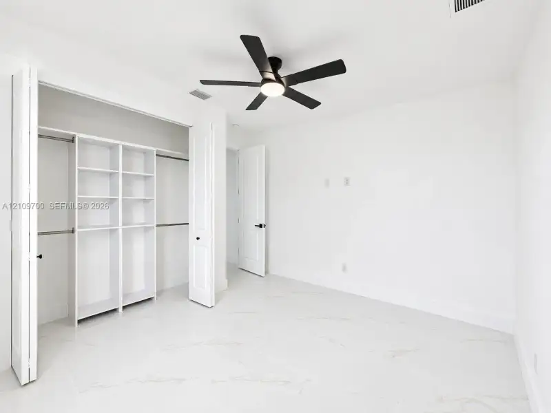 Interior space featuring large-format tile flooring with marble-pattern veining, a ceiling fan with integrated lighting, and a closet system with built-in shelving and dual hanging rods