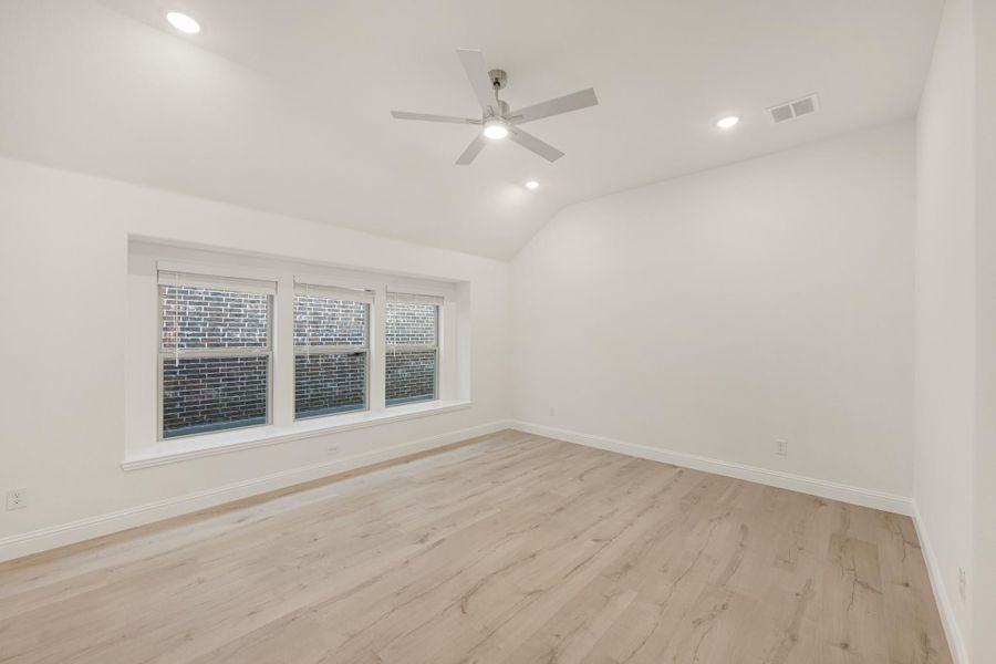 Empty bedroom with vaulted ceiling, ceiling fan, light wood floors, and triple window