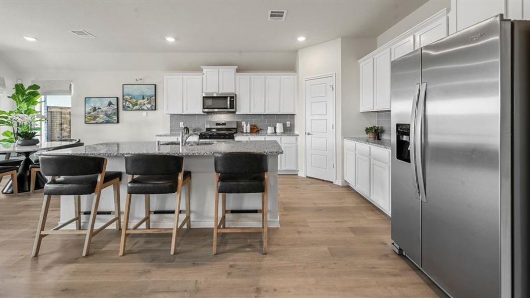 Kitchen featuring appliances with stainless steel finishes, white cabinetry, backsplash, light stone countertops, and light wood-style floors