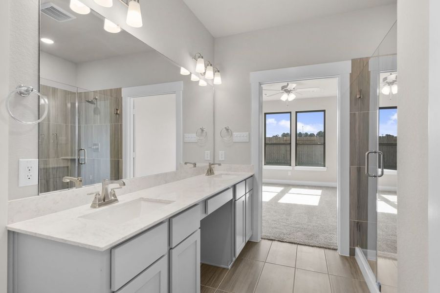 Image of a primary bath with a jack and jill vanity with light grey cabinets, white countertops, a large mirror and a standing shower