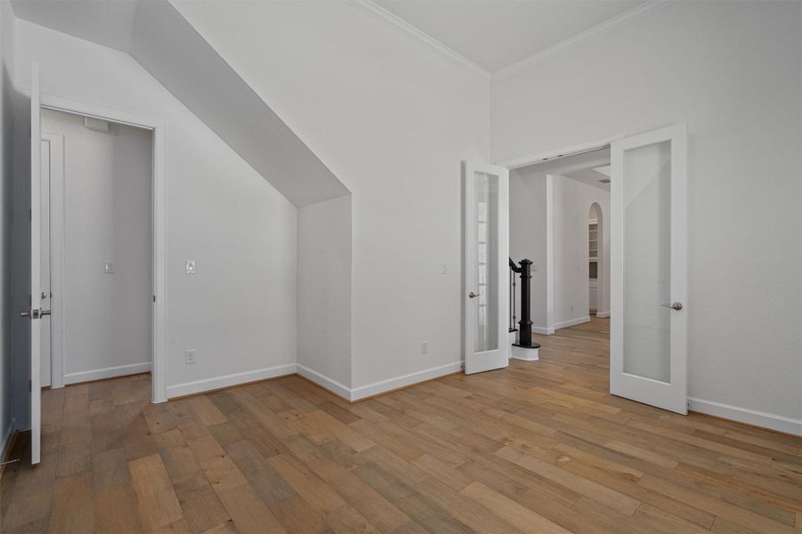 Spacious room featuring wood-finish flooring, white baseboards, and crown molding