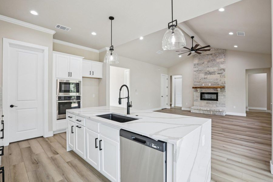 Kitchen with white cabinetry, appliances with stainless steel finishes, hanging light fixtures, light stone countertops, and light wood finished floors