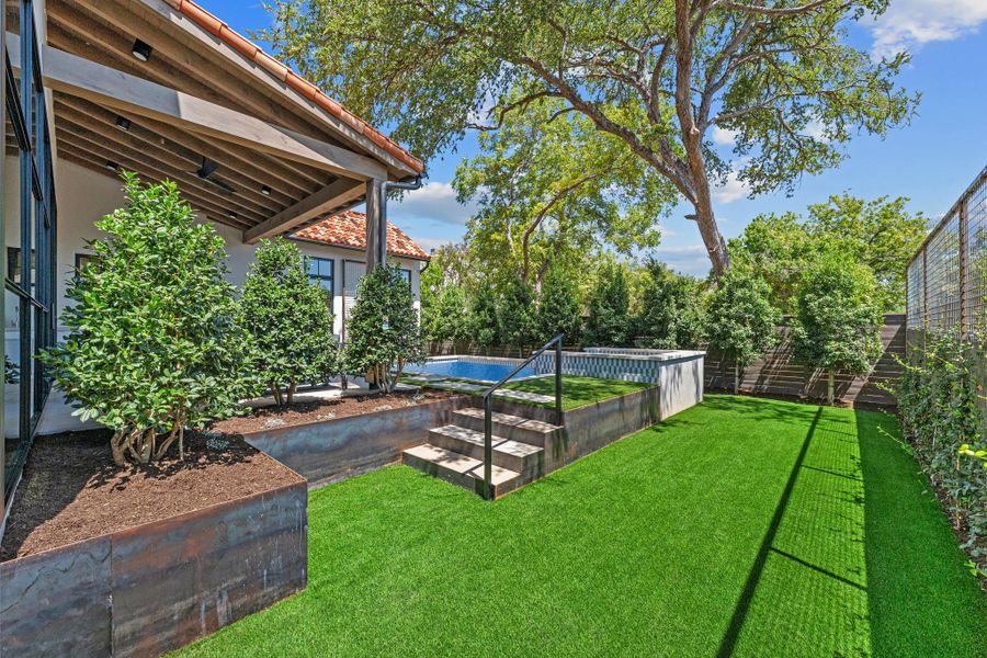 Exposed wood beams shelter the patio leading to a tiered lawn and swimming pool.