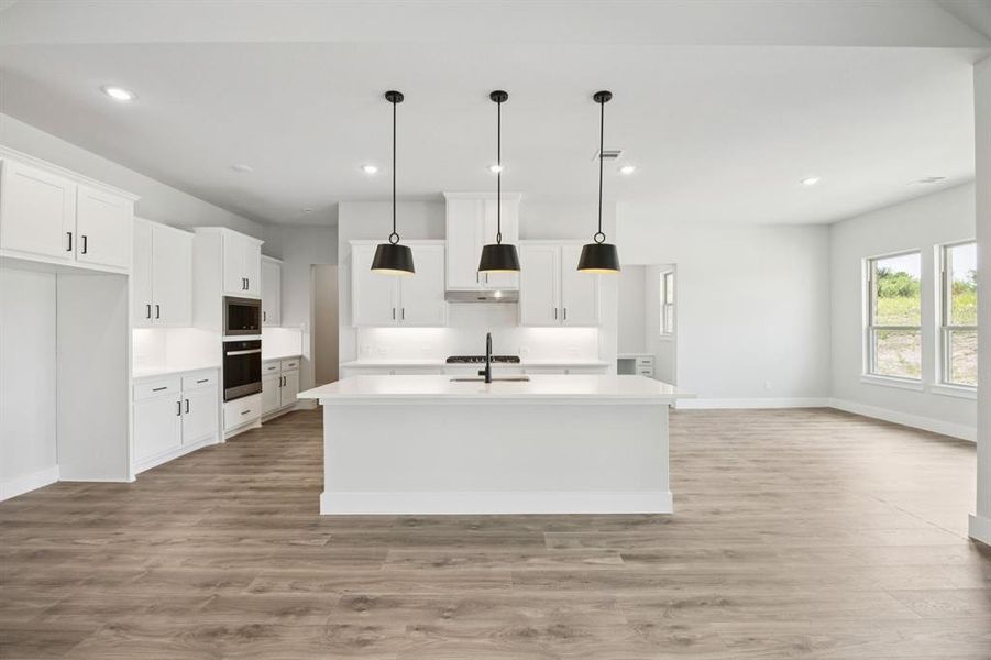 Kitchen with hanging light fixtures, white cabinetry, recessed lighting, a center island with sink, and light wood-type flooring