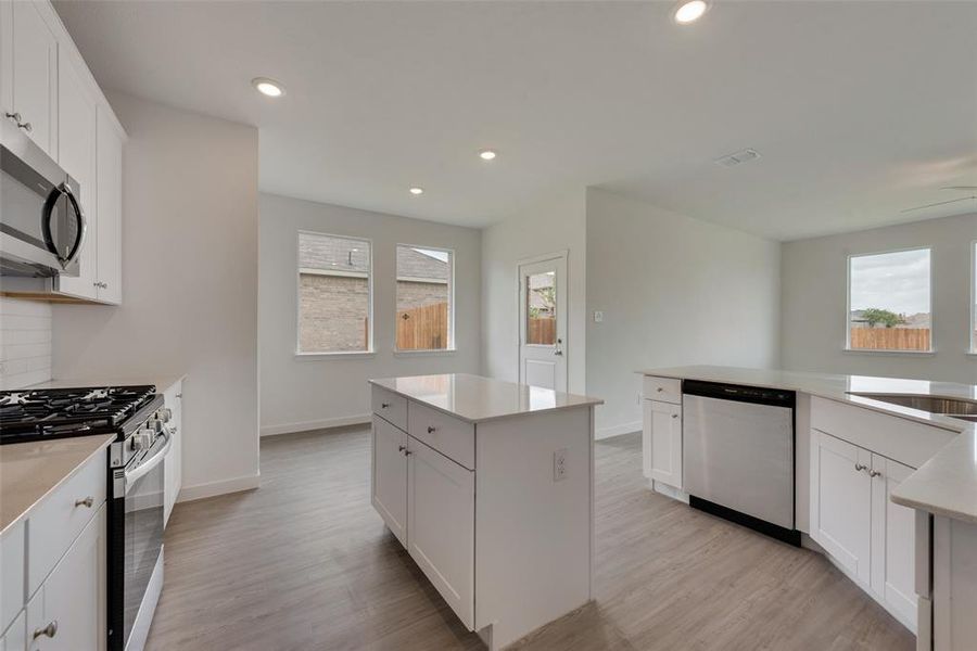 Kitchen with white cabinets, appliances with stainless steel finishes, light wood-type flooring, and a kitchen island