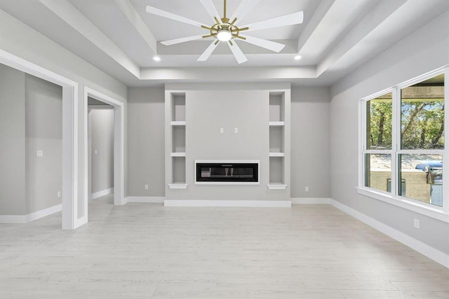 Unfurnished living room with a glass covered fireplace, light wood-type flooring, a tray ceiling, ceiling fan, and recessed lighting