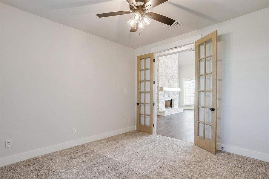 Carpeted empty room with ceiling fan, a fireplace, and french doors