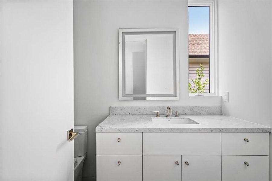 This elegant secondary ensuite bath boasts a luxurious Carrera marble vanity, complemented by sleek slate tile flooring. The spacious walk-in shower features ceramic linear tiles and a matching Carrera marble bench and shower surround, while the front-lit mirror adds a modern touch to this sophisticated space.