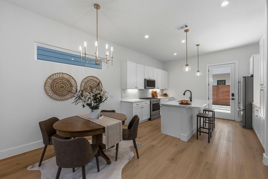 Kitchen featuring white cabinetry, stainless steel appliances, a center island with sink, and light wood finished floors