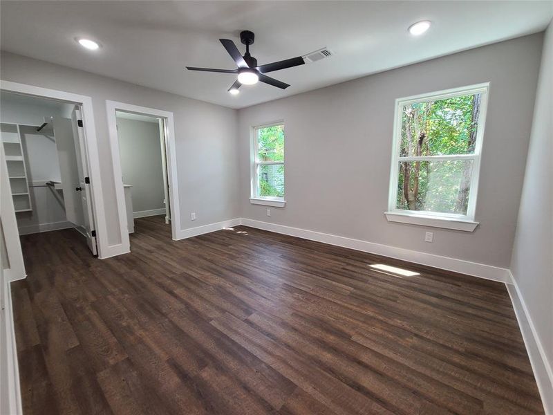 Unfurnished bedroom with ceiling fan, a spacious closet, dark wood-type flooring, and a closet