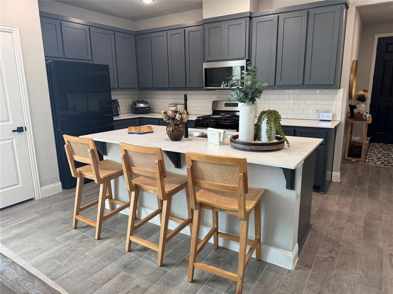 Kitchen featuring a kitchen bar, freestanding refrigerator, light wood-style flooring, a center island, and stainless steel microwave Kitchen featuring a kitchen bar, freestanding refrigerator, light wood-style flooring, a center island, and stainless steel microwave