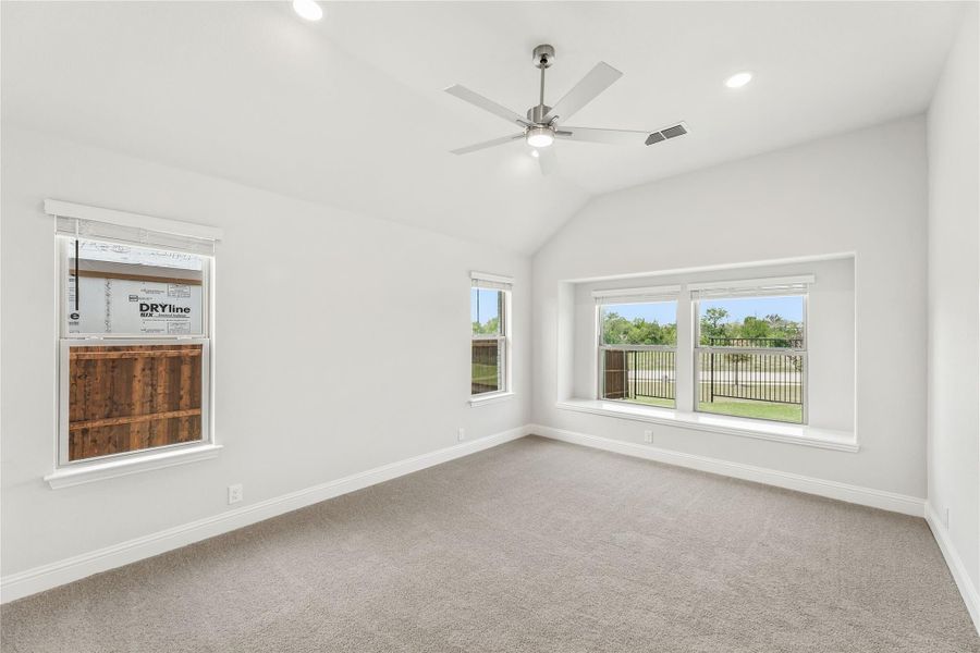 Empty bedroom with vaulted ceiling, ceiling fan, carpet flooring, and multiple windows with backyard views Empty bedroom with vaulted ceiling, ceiling fan, carpet flooring, and multiple windows with backyard views