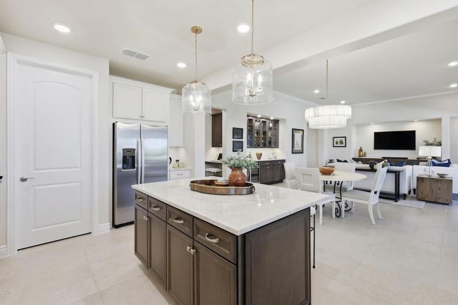 Kitchen featuring dark brown cabinets, stainless steel refrigerator with ice dispenser, light stone counters, hanging light fixtures, and open floor plan