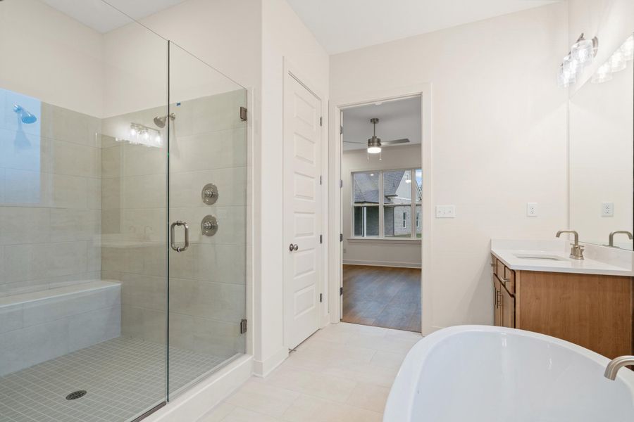 Bathroom featuring a glass-enclosed shower with a built-in bench, white tile flooring, a freestanding soaking tub, and a vanity with a white countertop and undermount sink Bathroom featuring a glass-enclosed shower with a built-in bench, white tile flooring, a freestanding soaking tub, and a vanity with a white countertop and undermount sink