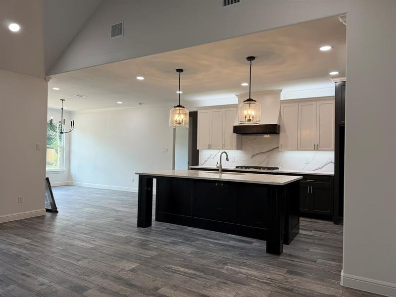 Open-concept kitchen featuring a large central island with a light-colored countertop, white upper cabinetry, dark lower cabinetry, and a patterned backsplash