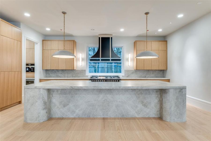 Kitchen with decorative light fixtures, light hardwood / wood-style floors, a spacious island, and exhaust hood