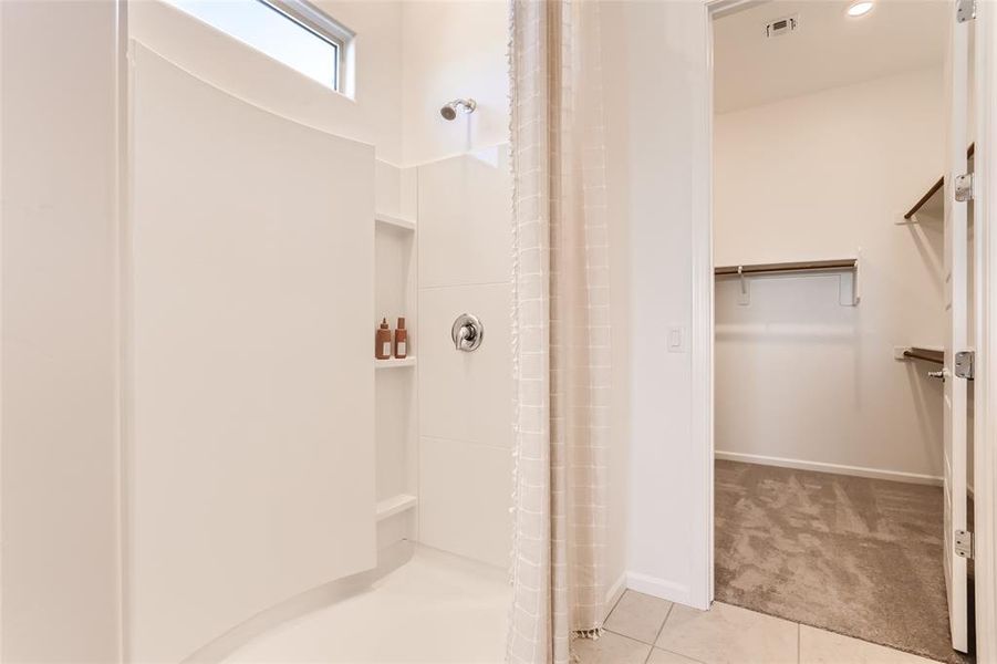 Full bath featuring a shower with shower curtain, a walk in closet, and light tile patterned flooring