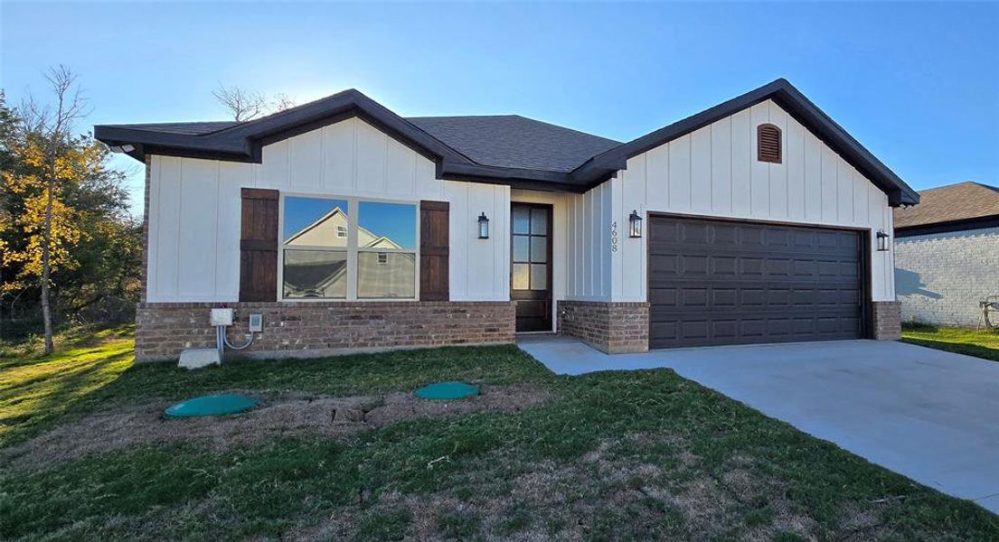 View of front of property with brick siding, board and batten siding, concrete driveway, an attached garage, and a front lawn