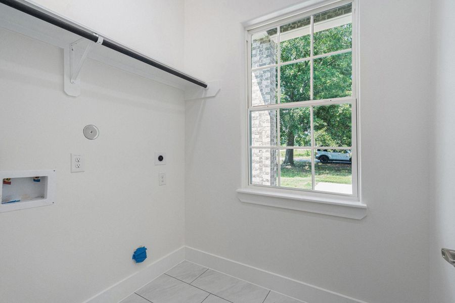 This photo shows a bright laundry room with a window providing natural light. It features hookups for a washer and dryer, tiled flooring, and a hanging rod for clothes. This photo shows a bright laundry room with a window providing natural light. It features hookups for a washer and dryer, tiled flooring, and a hanging rod for clothes.