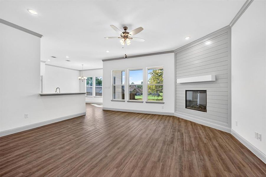 Unfurnished living room with crown molding, dark wood-type flooring, ceiling fan, a large fireplace, and a chandelier