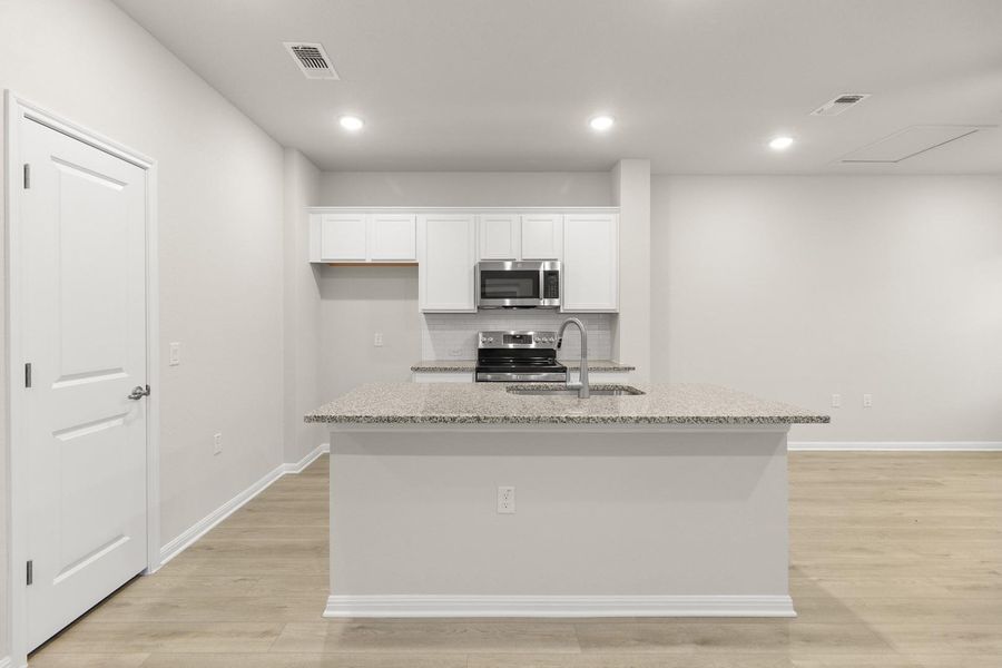 The kitchen features a large island with a sink, white cabinetry, stainless steel appliances, and light-colored flooring
