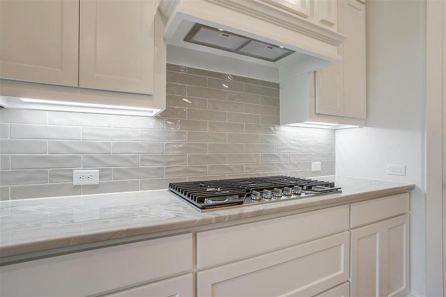 Kitchen featuring stainless steel gas cooktop, premium range hood, backsplash, and white cabinets