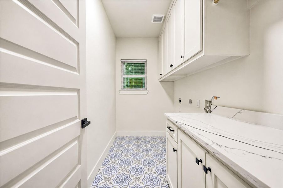 Stylish laundry room featuring elegant cabinetry, a sleek marble countertop, and eye-catching patterned tile flooring.