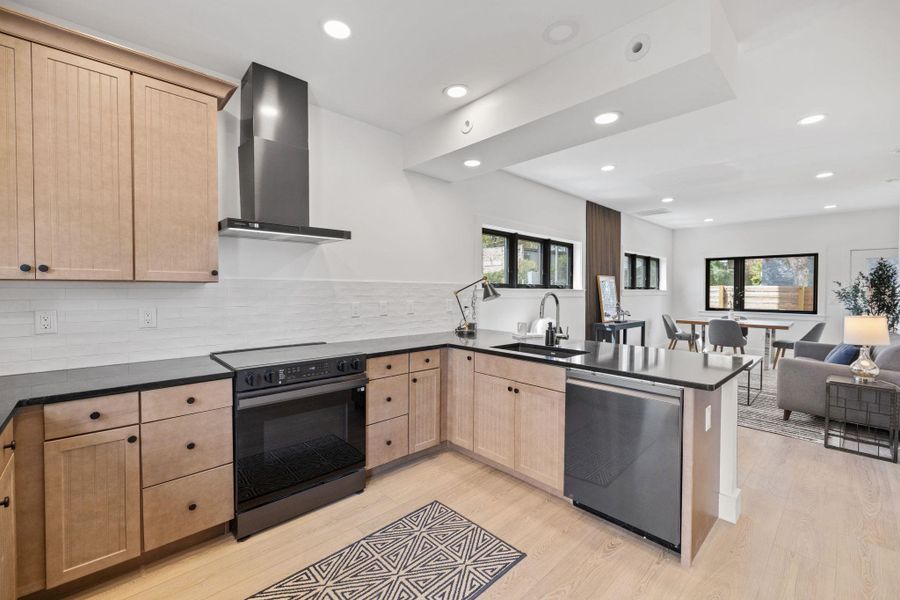Kitchen with a peninsula, open floor plan, black range with electric cooktop, wall chimney exhaust hood, and dishwasher