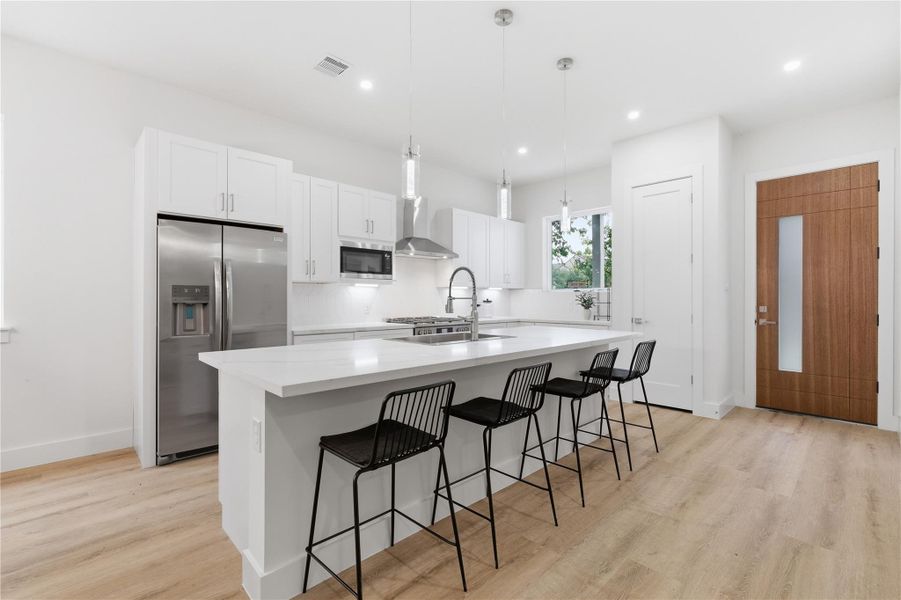 The kitchen has ample natural light and contemporary pendant lighting, complemented by light wood tone floors.