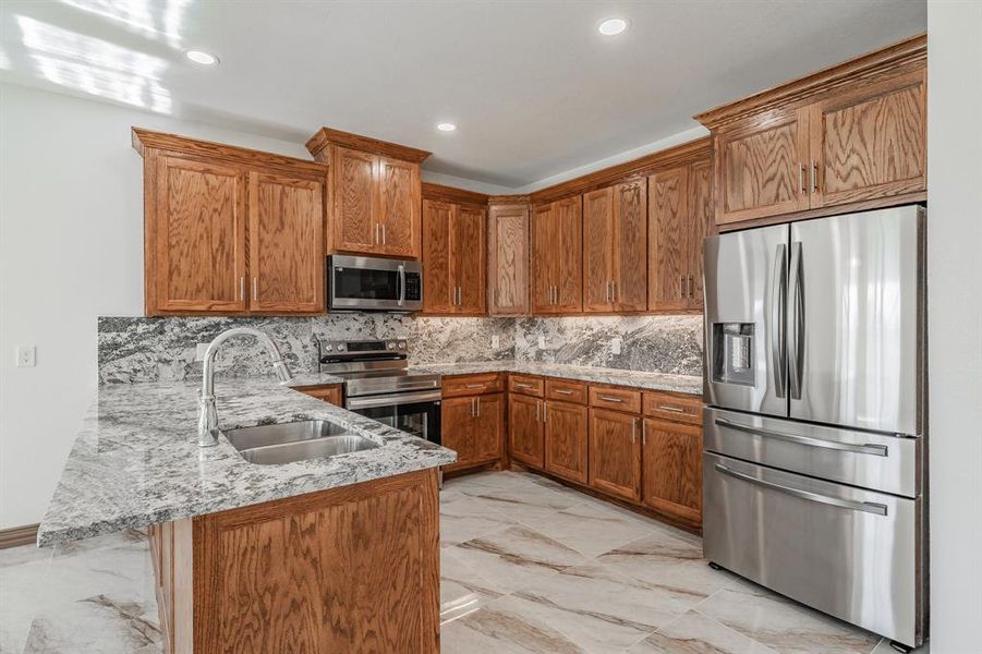 Kitchen with a peninsula, a sink, marble finish floor, appliances with stainless steel finishes, and brown cabinets