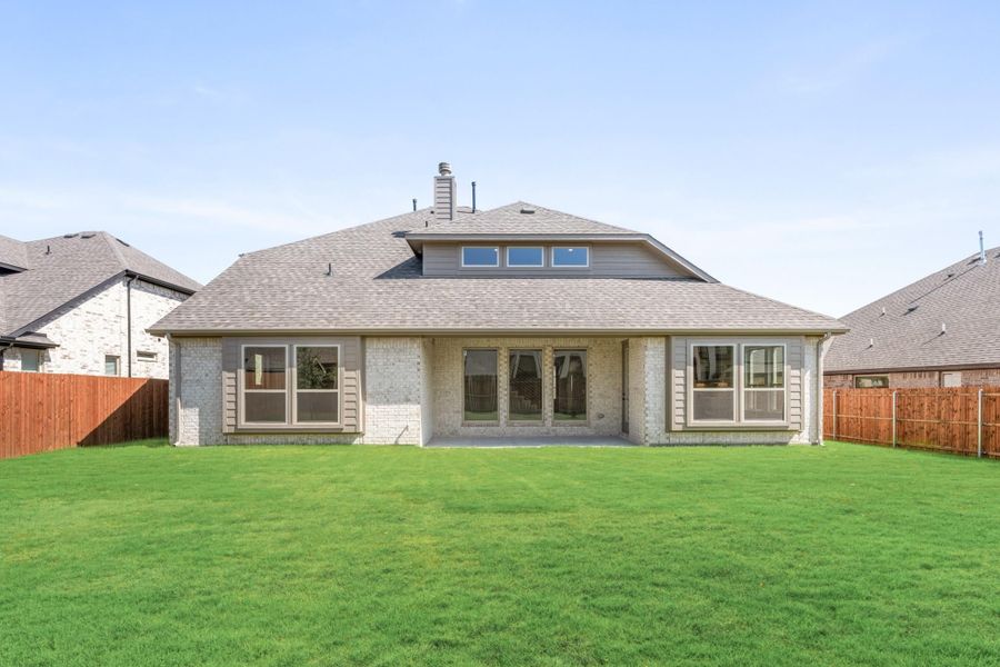 Rear view of single-story brick home with large backyard, patio, and wood privacy fence