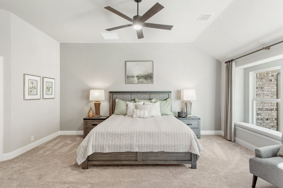 Spacious bedroom with vaulted ceiling, ceiling fan, wood bed frame, and neutral carpet flooring