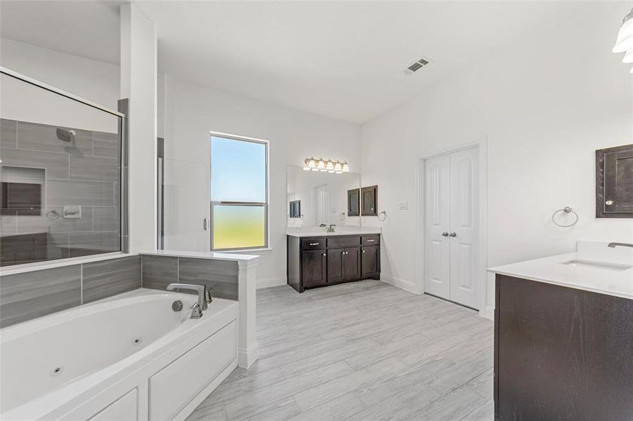 Bathroom featuring baseboards, a whirlpool tub, two vanities, and a tile shower