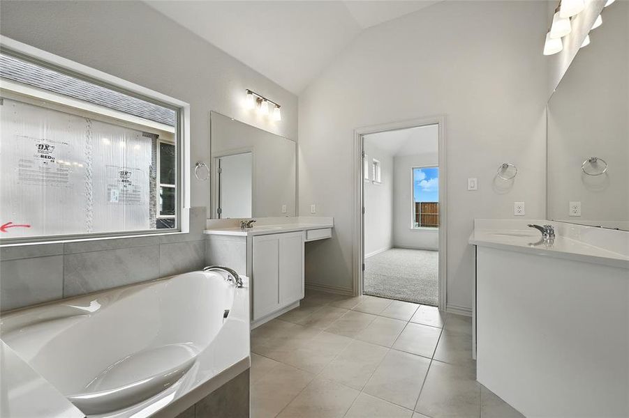 Full bathroom with lofted ceiling, two vanities, light tile patterned flooring, and a garden tub