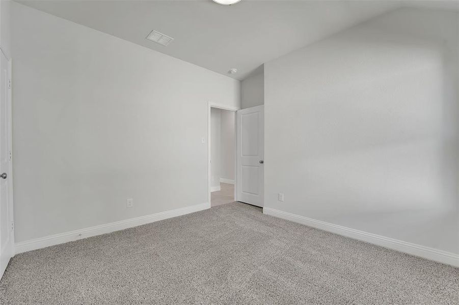 Unfurnished bedroom with lofted ceiling, light carpet, visible vents, and baseboards