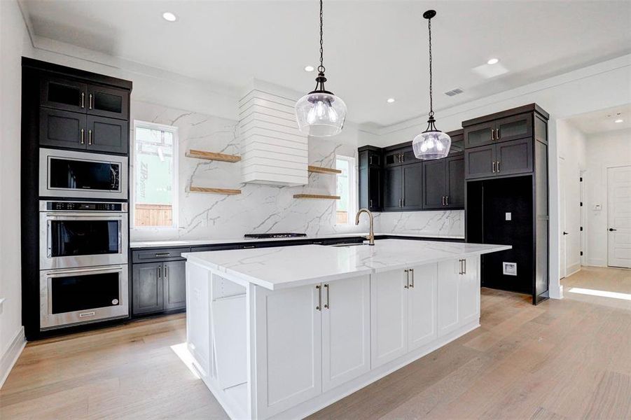 Kitchen featuring tasteful backsplash, light wood-type flooring, stainless steel microwave, light stone counters, and a center island with sink