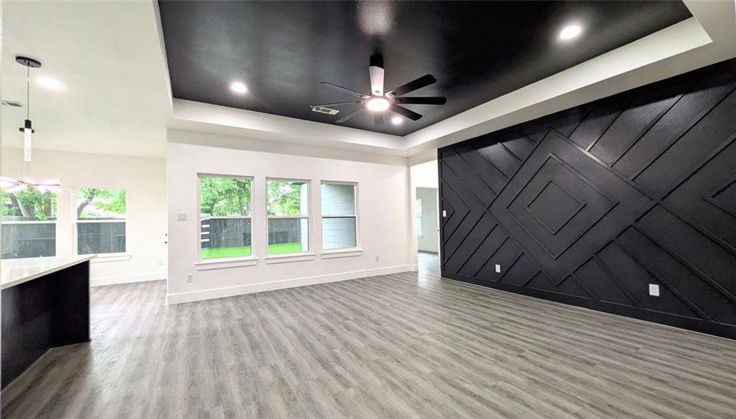 Unfurnished living room featuring baseboards, a ceiling fan, a tray ceiling, and wood finished floors