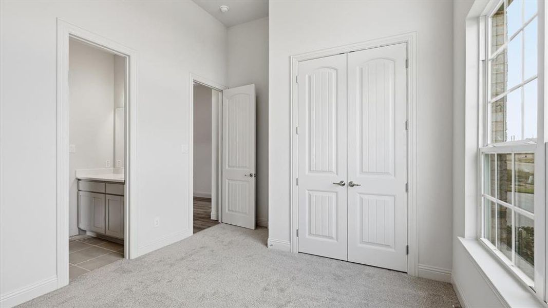 Carpeted room featuring a double-pane window with white trim, a double-door closet with paneling, and an entryway to a bathroom with a vanity and tile flooring