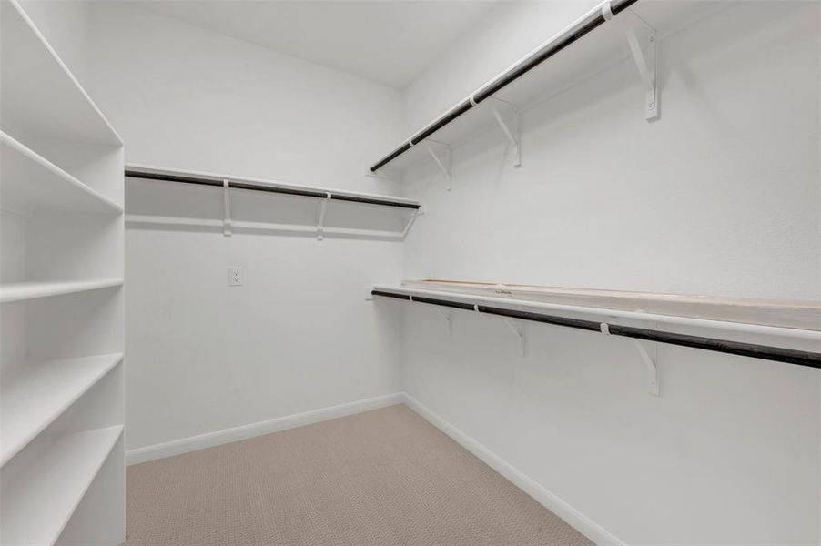 Walk-in closet featuring built-in shelving, multiple hanging rods, overhead storage shelves, and neutral carpeting Walk-in closet featuring built-in shelving, multiple hanging rods, overhead storage shelves, and neutral carpeting