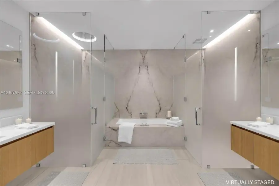 Dual floating wood-finish vanities with rectangular integrated sinks, stone-clad drop-in bathtub with wall-mounted faucet, full-height stone backsplash, and frameless glass-enclosed shower stalls with recessed overhead lighting Dual floating wood-finish vanities with rectangular integrated sinks, stone-clad drop-in bathtub with wall-mounted faucet, full-height stone backsplash, and frameless glass-enclosed shower stalls with recessed overhead lighting