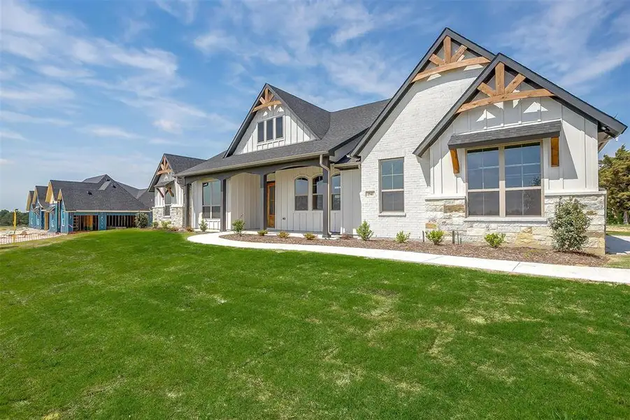 Modern inspired farmhouse featuring board and batten siding, a shingled roof, a front lawn, and stone siding