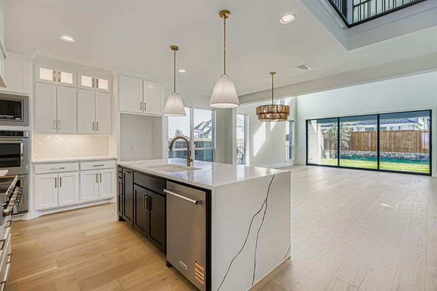 Kitchen featuring healthy amount of natural light, white cabinets, an island with sink, decorative light fixtures, and recessed lighting