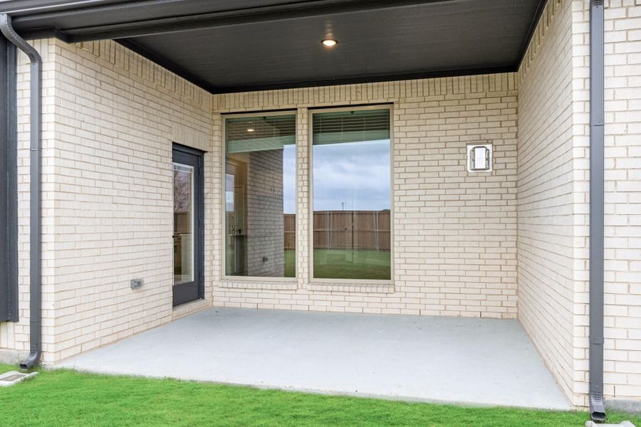 Covered back patio with concrete floor, brick exterior, large windows, and a back door leading inside