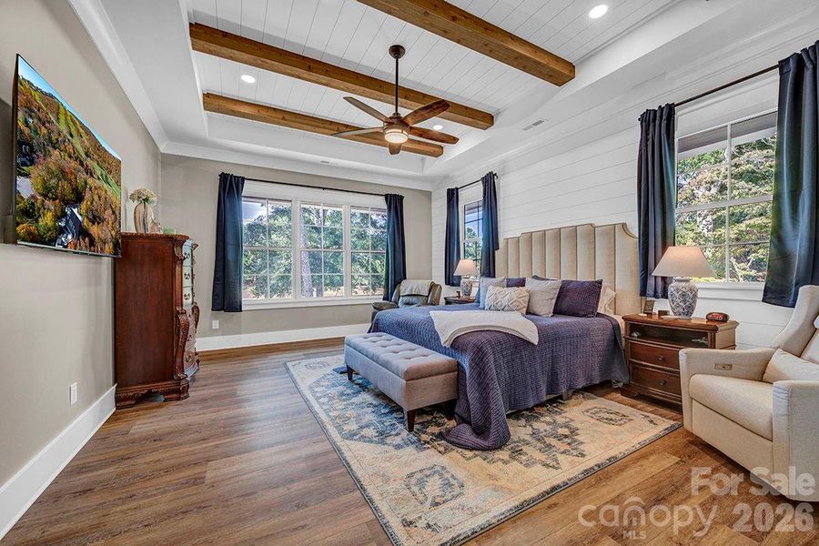 Main Level Primary Suite Bedroom. Ship lap accent wall, Tongue & Groove tray ceiling w/beams and ceiling fan.