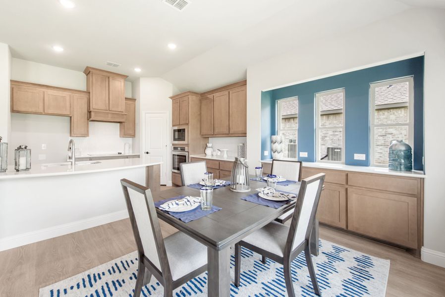 Dining area with four-seat table adjacent to kitchen with light wood cabinets and blue accent wall