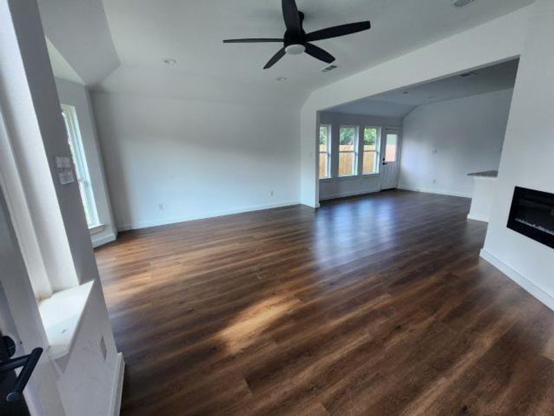 Unfurnished living room with dark wood-style flooring, lofted ceiling, a glass covered fireplace, and ceiling fan Unfurnished living room with dark wood-style flooring, lofted ceiling, a glass covered fireplace, and ceiling fan