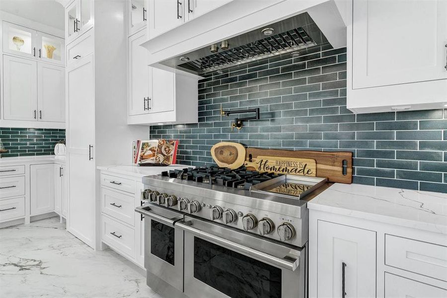 Kitchen with light stone countertops, white cabinets, tasteful backsplash, and double oven range